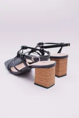 Sandalias negras de ecocuero con tiras finas que se cruzan en la capellada y se atan con nudos. Taco cuadrado simil madera.