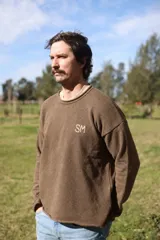 Sweater marrón de tejido de punto con mangas largas, cuello redondo y detalle bordado con las iniciales SM en el pecho.