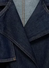 Abrigo corto estilo chaqueta de jean, confeccionado en algodón denim azul oscuro. Presenta cuello con solapas, cierre frontal, trabillas en los hombros y mangas largas con trabillas ajustables.