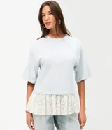 Remera overboxy de algodón color celeste, con cuello redondo, mangas cortas amplias y bajo asimétrico con aplicación de encaje blanco.