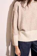 Sweater de punto con cuello alto, corte holgado y diseño color block en tonos beige y blanco.
