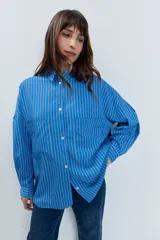 Camisa de corte oversize con estampado de rayas verticales, cuello clásico, cierre frontal con botones y mangas largas con volumen.