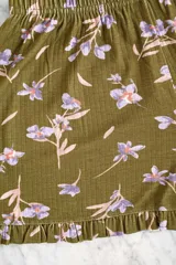Conjunto de pijama verde oliva con estampado de flores lilas, compuesto por un top de mangas cortas con escote en V y un short con cintura elástica y volados en el ruedo.