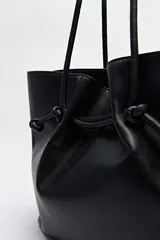 Bolso tipo tote bag negro de cuero sintético, con frunce superior ajustable con cordones y doble asa de hombro.