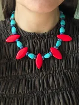 Collar corto con diseño de cuentas alternadas en forma de gota y elipse, combinando piedras turquesas veteadas, cuentas azules pequeñas y piezas centrales alargadas de color rojo intenso.