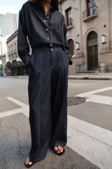 Jeans de tiro alto color azul oscuro, con cintura elástica en la espalda, bolsillos delanteros y bolsillos de plastrón en la espalda. Presenta pernera ancha y cierre frontal con cremallera y botón a presión.