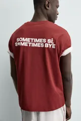 Camiseta blanca de corte relajado (relaxed fit) con cuello redondo y manga corta. Presenta un bolsillo plastrón en el pecho y un estampado de texto en color marrón rojizo en la espalda que dice "SOMETIMES SÍ, SOMETIMES BYE" (reemplazando la 'O' de 'SOMETIMES' por un corazón).