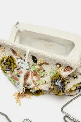 Bolso tipo pouch rígido, con cuerpo cubierto de abalorios, cuentas y apliques florales en tonos verdes, beige y dorados. Cuenta con cierre de botón imantado y cadena extraíble para usar como bandolera.