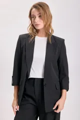 Blazer negro de corte sastrero con mangas tres cuartos, solapas clásicas y cierre frontal con un botón. Presenta bolsillos laterales con solapa.