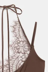 Body negro de tejido elástico con escote redondo y tirantes finos. Presenta un panel superior de encaje floral a tono con diseño halter ajustable mediante lazada en el cuello y cierre inferior con botones a presión.