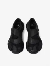Zapatilla urbana de diseño vanguardista en color negro, con estructura de malla y superposiciones de paneles de goma texturizados. Presenta cierre con tiras autoadherentes y suela robusta con diseño ergonómico.