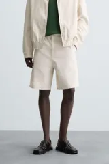 Bermuda de algodón color beige claro con rayas verticales finas en tono más oscuro. Diseño de corte regular con bolsillos delanteros y bolsillos traseros de plastrón.