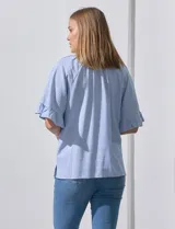 Blusa celeste y blanca a rayas verticales, de lino y corte holgado. Tiene cuello redondo con escote en V y lazo de ajuste. Las mangas son cortas y amplias, con volados en el borde.