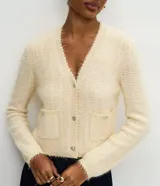 Cardigan de punto con textura de pelitos, cuello en V y cierre frontal con botones metalizados. Presenta mangas largas y dos bolsillos frontales pequeños. Diseño de corte regular.