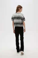 Cardigan de punto con diseño de rombos en tonos gris, blanco y negro. Presenta cuello redondo, cierre frontal con botones y mangas cortas.