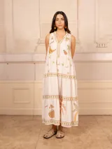 Vestido largo color crema con estampado de flores y corazones en tonos azules, naranjas y amarillos. Tiene cuello en V con ribete azul y corte imperio con falda escalonada.