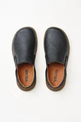 Zapatillas tipo slip-on de gamuza color beige, con diseño barefoot y suela de corcho texturizado. Presenta elásticos laterales negros para un calce fácil.