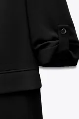 Blazer negro de corte recto, con cuello solapa y hombreras. Las mangas son tres cuartos con vuelta asegurada por un botón dorado. Posee bolsillos delanteros con solapa.