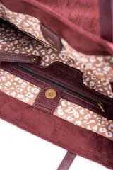 Bolso tipo tote de gran tamaño en color bordó, confeccionado en material con textura similar a la gamuza. Cuenta con doble asa larga para llevar al hombro y una pequeña placa metálica decorativa en el frente.