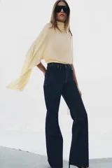 Jeans de tiro alto con corte flare y ajuste slim. Presenta trabillas en la cintura, bolsillos delanteros con detalle de botones metálicos y raya planchada a lo largo de las piernas. Cierre frontal con cremallera y botón.
