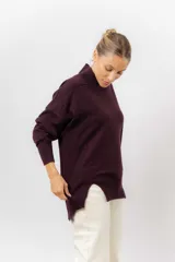 Sweater de tejido de punto color beige, con cuello alto, hombros caídos, mangas largas con puños acanalados y tajos laterales en el ruedo.