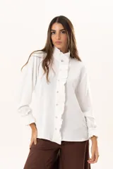 Camisa blanca de cuello alto con volados frontales a lo largo de la botonadura, manga larga con puños con volados y cierre frontal con botones.