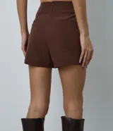 Short pollera corto de sastrería color marrón, con diseño cruzado redondeado en el frente y cierre invisible en la espalda.