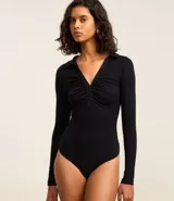 Body negro de rib, con cuello polo, escote en V, mangas largas y frunces en el busto. Cierre inferior con botones a presión.