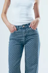 Pantalón de jean corte wide leg, color beige con estampado de rayas verticales finas. Presenta tiro alto, cierre frontal con botón y bolsillos laterales.