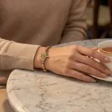 Pulsera de acero con baño de oro, compuesta por esferas doradas y oscuras, con un dije central en forma de árbol de la vida decorado con cristales multicolores.