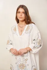Vestido corto de color blanco con escote en V, mangas 3/4 y diseño amplio, adornado con bordados artesanales en tonos beige, negro y celeste.