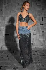 Falda larga de tiro alto, confeccionada en tela elástica cubierta de lentejuelas negras. Presenta una sección superior de denim con bolsillos y corte a la cadera.