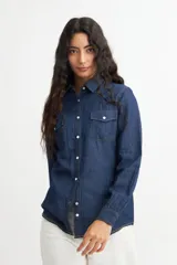 Camisa de denim azul con dos bolsillos frontales con botón, corte recto y mangas largas con puños abotonados.