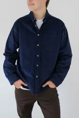 Camisa azul marino de pana, de corte relajado y silueta recta, con cuello clásico abotonado, cierre frontal con botones, mangas largas y un bolsillo aplicado en el pecho.