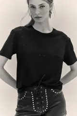 Remera negra de manga corta con cuello redondo, decorada con pequeñas aplicaciones brillantes dispersas en la parte frontal y mangas.