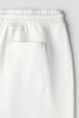 Pantalón deportivo de felpa color blanco roto, con interior cepillado suave. Presenta elástico revestido y cordón ajustable en la cintura, bolsillos laterales y puños acanalados. Corte relajado.