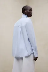 Camisa de corte holgado en color celeste, con cuello camisero clásico, cierre frontal de botones, manga larga con puños rectos y bajo redondeado.