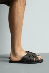 Sandalia plana de hombre confeccionada en piel color negro, con diseño de tiras cruzadas y entrelazadas en el empeine.