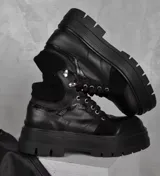 Borcegos de cuero vacuno color negro, con suela track de plataforma alta, cordones frontales con ganchos metálicos y combinación de texturas en cuero liso y gamuza.