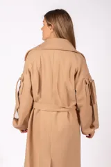 Tapado largo de paño color beige, con solapas amplias, cierre frontal cruzado con cinturón ajustable y detalles de tiras decorativas en las mangas.