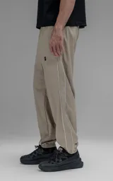 Pantalón deportivo de microfibra color beige, con corte regular y diseño de inspiración vintage. Presenta vivos laterales a contratono, cintura elástica y puños elásticos en los tobillos.