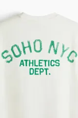 Remera de corte holgado en punto de algodón, con cuello redondo acanalado y hombros caídos. Presenta un estampado frontal con la inscripción Soho NYC Athletics Dept. en color verde.