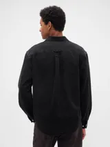 Camisa de jean de corte clásico en color azul oscuro, con cierre frontal de botones, cuello camisero y dos bolsillos frontales con solapa y botón.