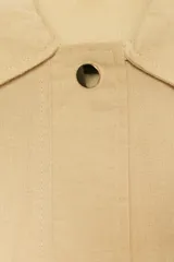 Chaqueta color beige con cuello solapa, manga larga remangada con trabilla y botón, y bolsillos de plastrón en el delantero. Cierre frontal con botones.