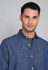 Camisa de jean azul con botones blancos, mangas largas con puños doblados y corte clásico.