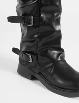 Botas altas de caña media en color negro, confeccionadas en cuero sintético con acabado ligeramente arrugado. Presentan un diseño con tres correas horizontales ajustables mediante hebillas metálicas plateadas y suela de caucho con plataforma baja.
