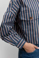 Camisa de corte oversize con diseño de rayas verticales en tonos azul y blanco, cuello clásico, cierre frontal con botones y mangas largas con puños abotonados.