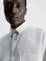 Camisa blanca de manga larga con cuello clásico, cierre frontal con botones, bolsillo de parche en el pecho y logo CK bordado en el bolsillo.