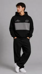 Hoodie negro de corte relajado, con una franja horizontal gris en el pecho, capucha ajustable y bolsillo tipo canguro. Presenta pequeños estampados en tipografía blanca y un logotipo abstracto en la parte superior.