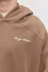Canguro marrón con capucha, bolsillo frontal tipo kango y diseño oversize de corte relajado con mangas largas.